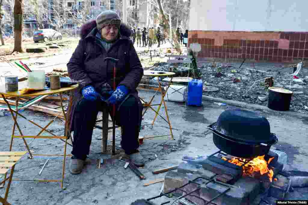 Жінка готує їжу на відкритому вогні у житловому кварталі, пошкодженого російськими обстрілами. Люди намагаються розтопити сніг, щоб отримати питтєву воду.&nbsp;Маріуполь, 19 березня 2022 року